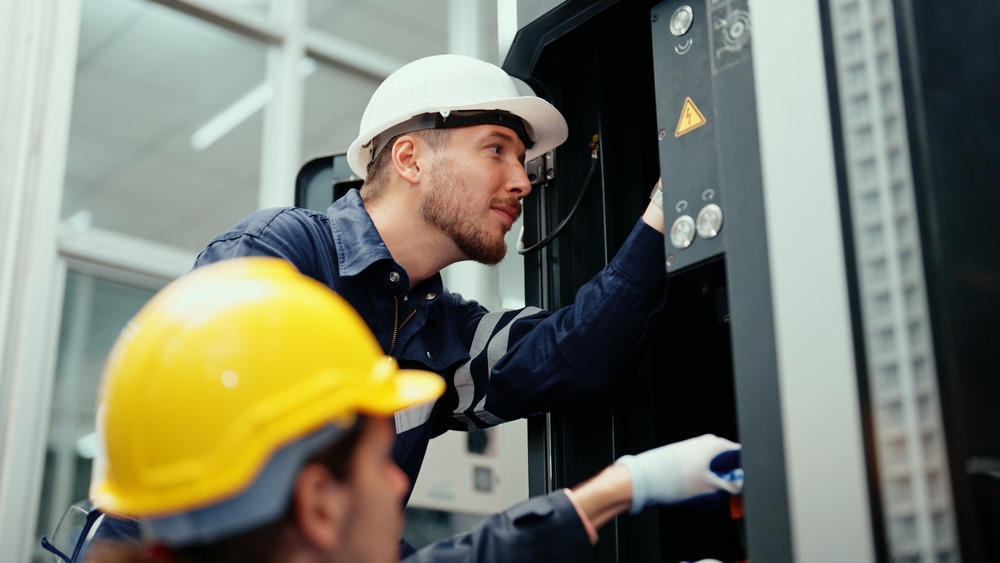 two men in safety wear are assisting in adjusting and maintaining CNC machine in the factory.