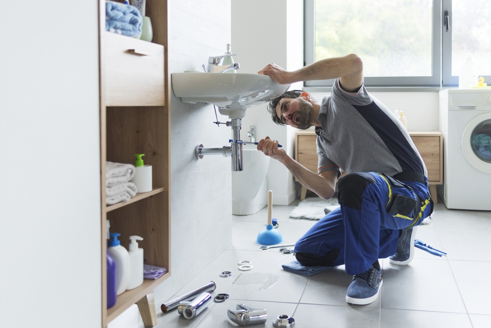 Professional plumber using pliers to check drain pipes at home, demonstrating how plumbing field service software improves on-site efficiency